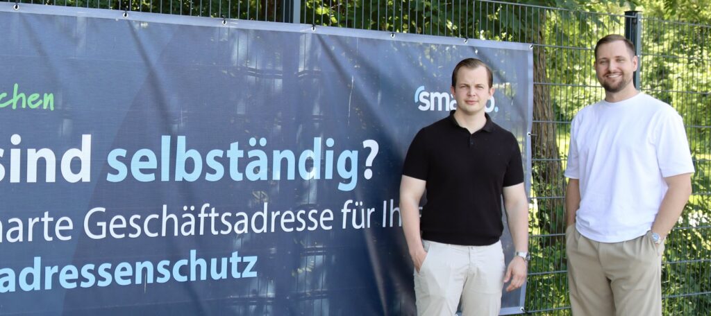 Zwei Gründer vor dem Smarvo Werbebanner am Spielfeldrand des 1. FC Kamp-Lintfort