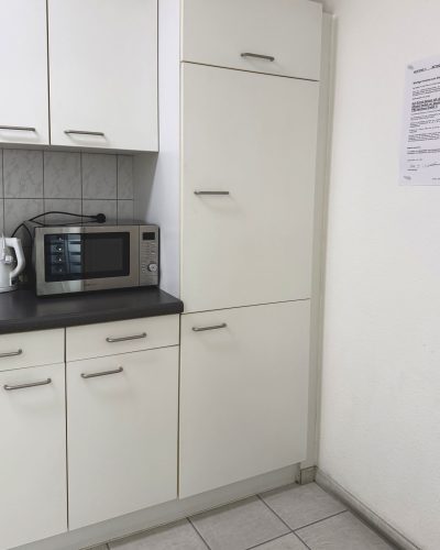 Weiße Einbauküche im Büro mit Kühlschrank, Kochfeld, Mikrowelle, Wasserkocher und mehr