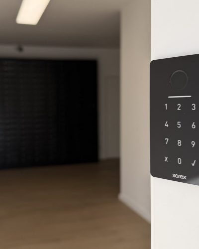 Modernes Zutrittssystem mit Zahlencode-Tastatur im Smarvo Gebäude, montiert an einer weißen Wand mit Holzfußboden und Briefkastenanlage im Hintergrund.